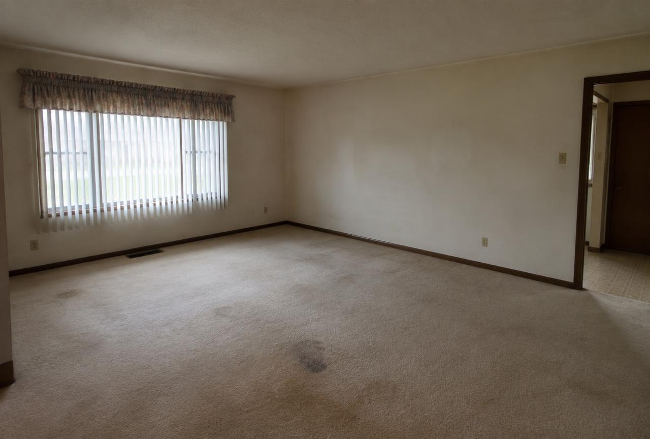 Worn, stained beige carpet in an empty older living room before new flooring.