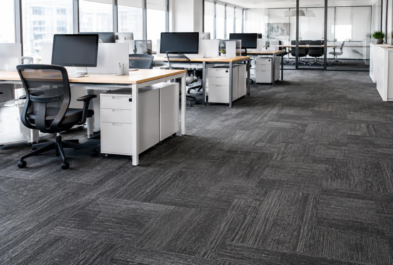 Charcoal grey modular carpet tile flooring installed through a modern open office with desks.