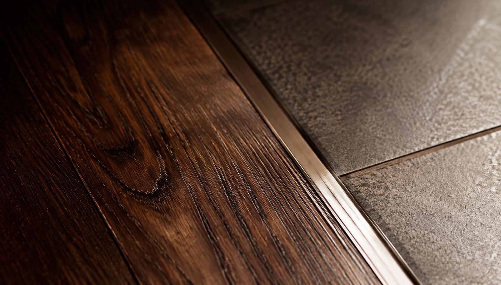 Close-up of dark wood plank grain meeting tile at a clean metal transition strip.
